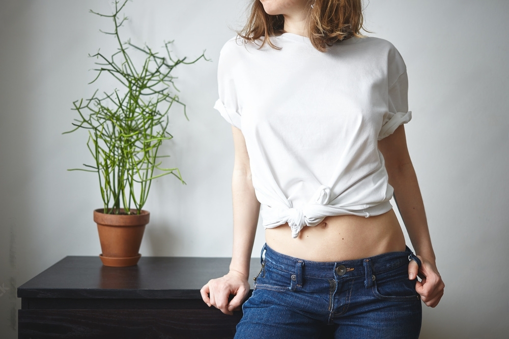 Girl standing nearby the table and wear it oversized t-shirt in knotted style with blue jeans